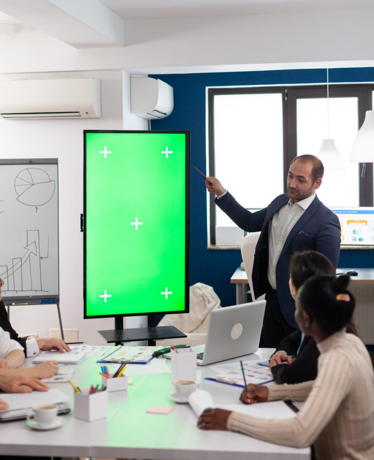 Leader of company presenting financial plan using mockup display in front of diverse team brainstorming. Manager explainig project strategy on green screen monitor with chroma key desktop in boardroom